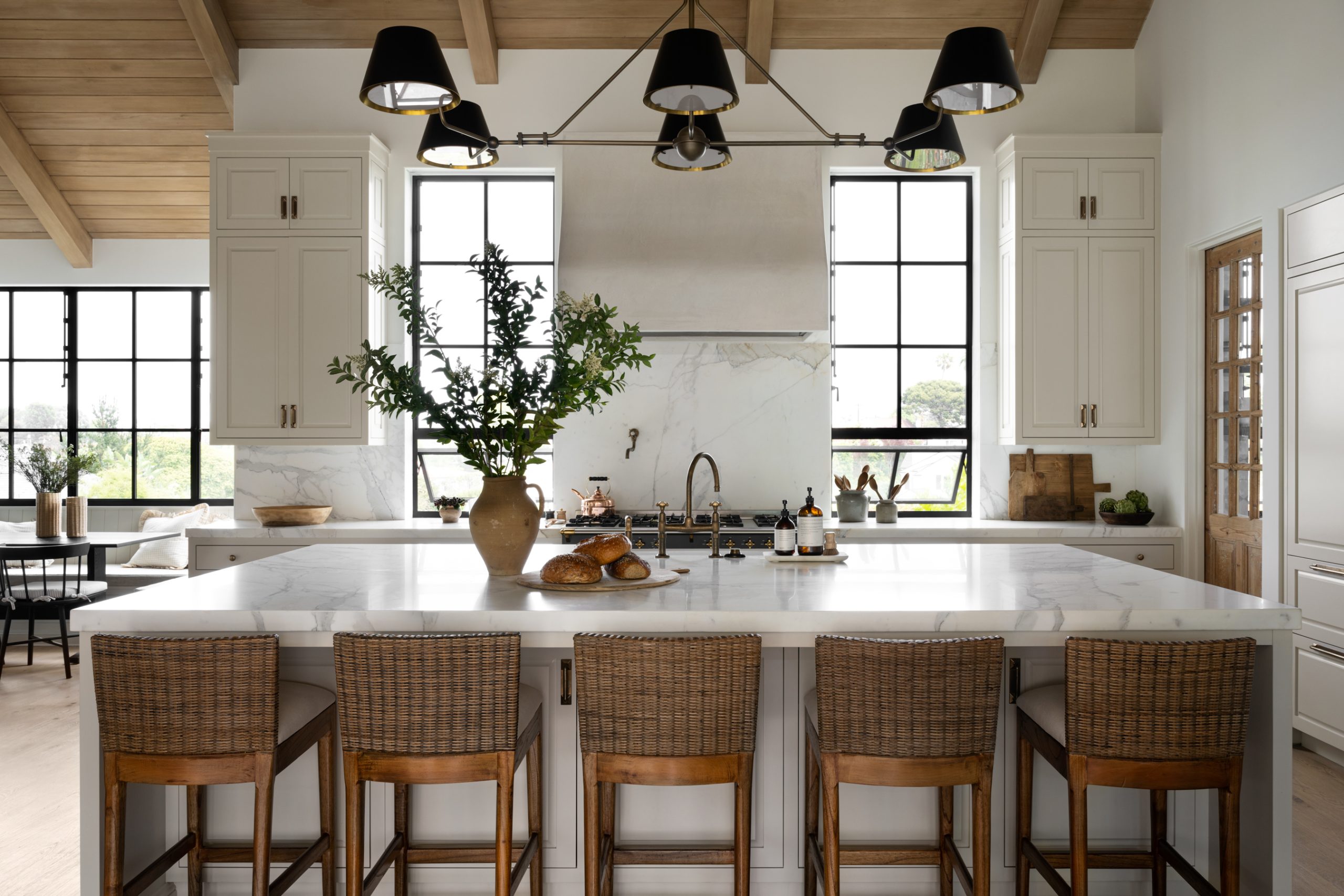Kitchen with white cabinetry and white marble countertops with woven counter stools