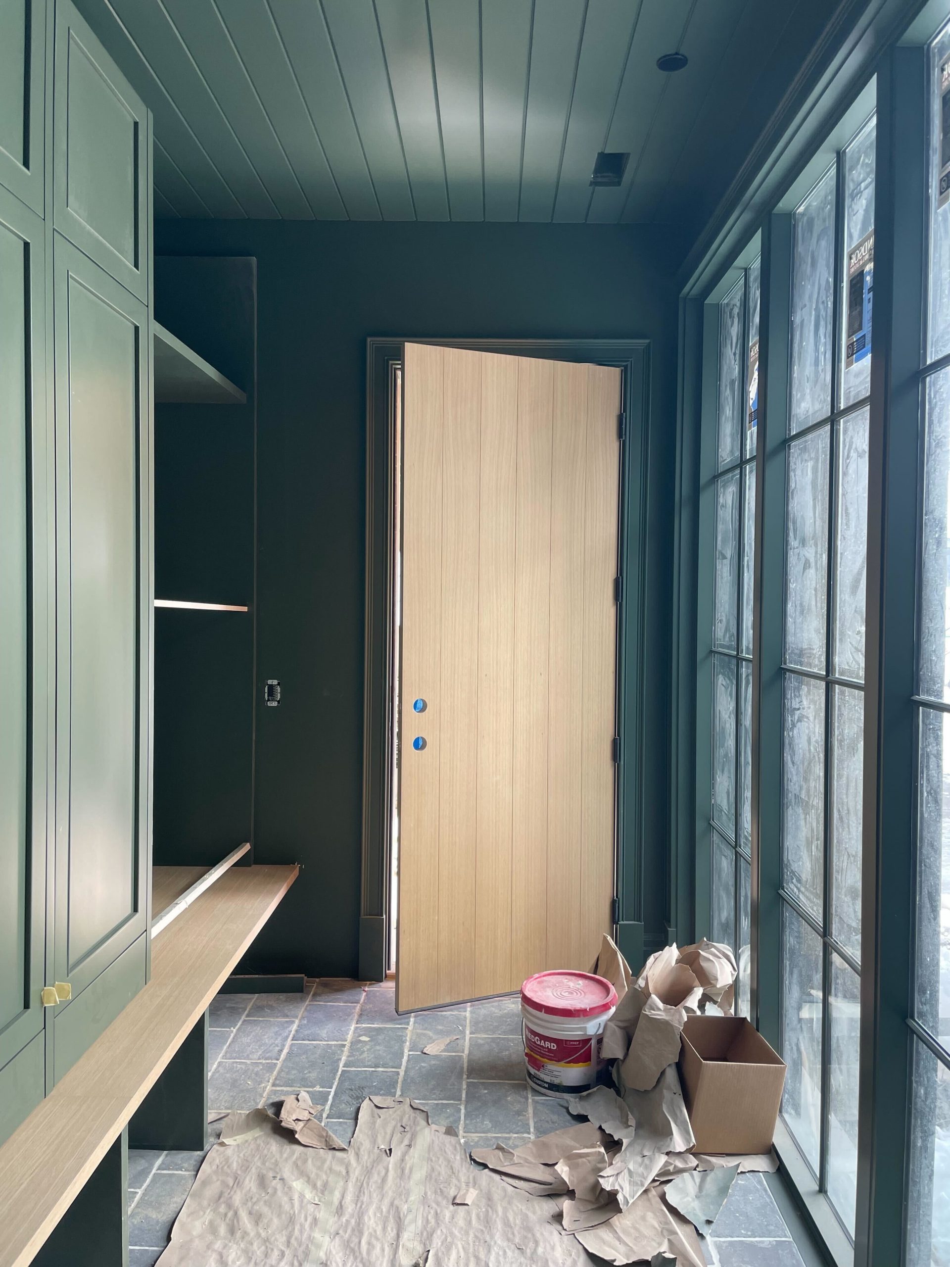 Green mudroom with windows and tan door in construction phase
