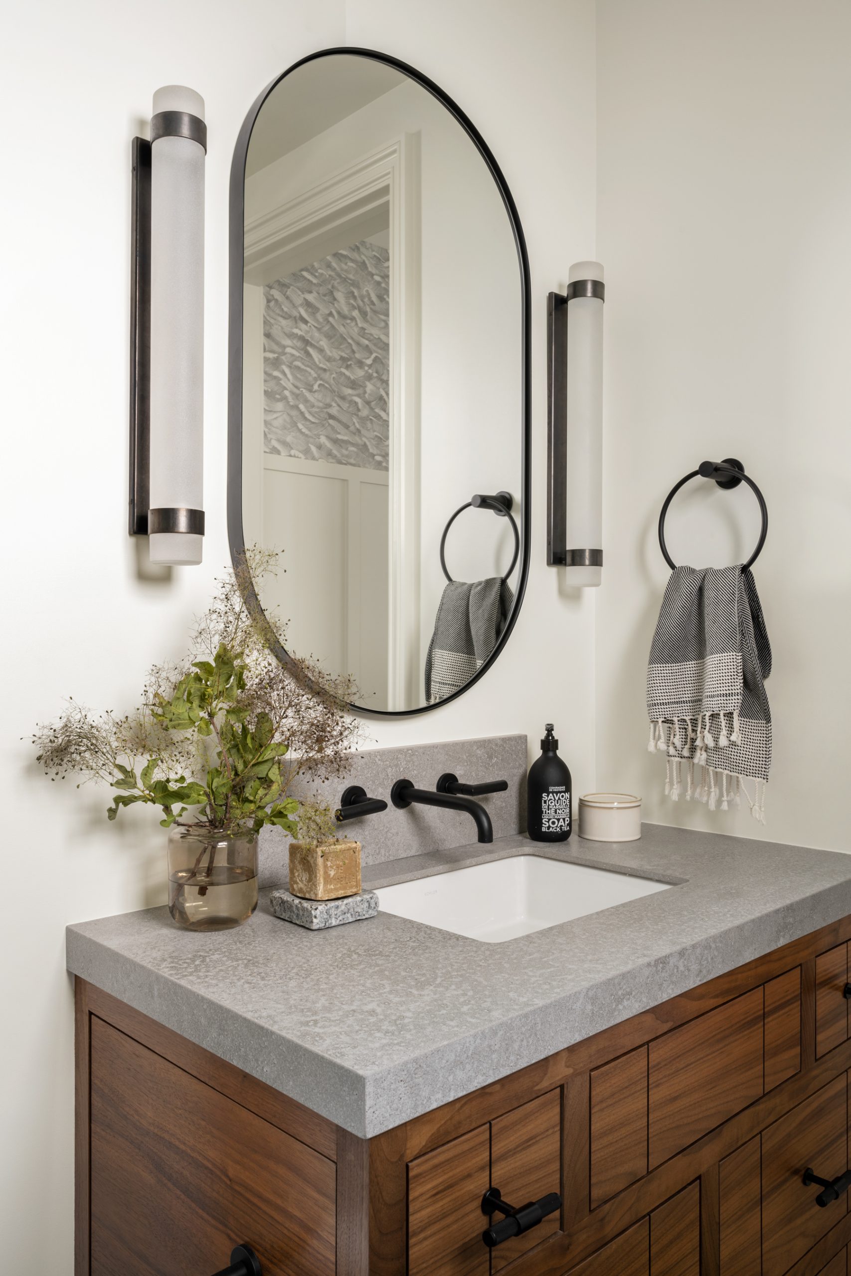 bathroom with dark wood cabinet and gray countertop with sconces on the side of oval mirror