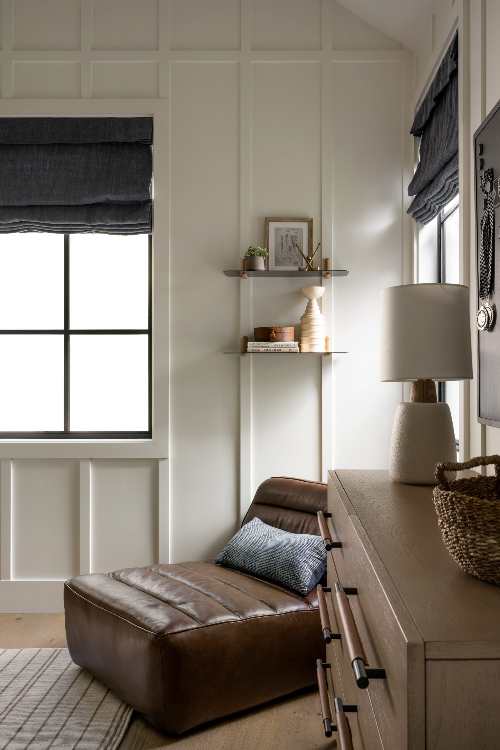 bedroom with white paneling with leather lounger with two shelves hanging above
