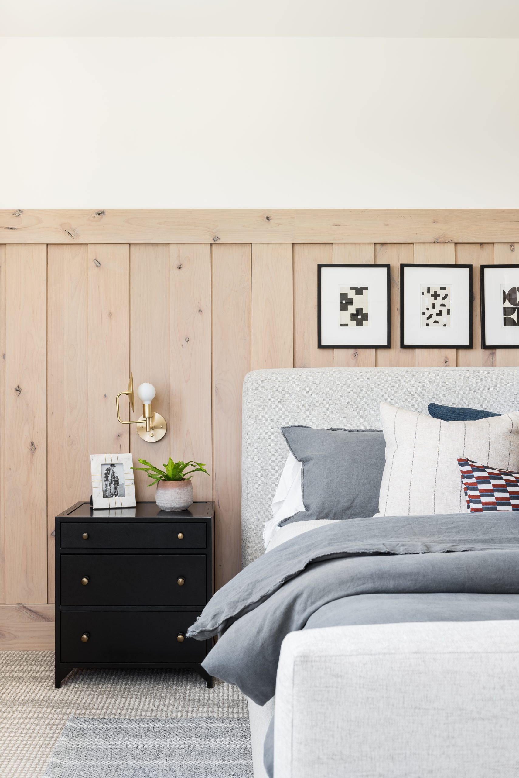 bedroom with wood paneling and upholstered bed with black nightstands and brass sconces