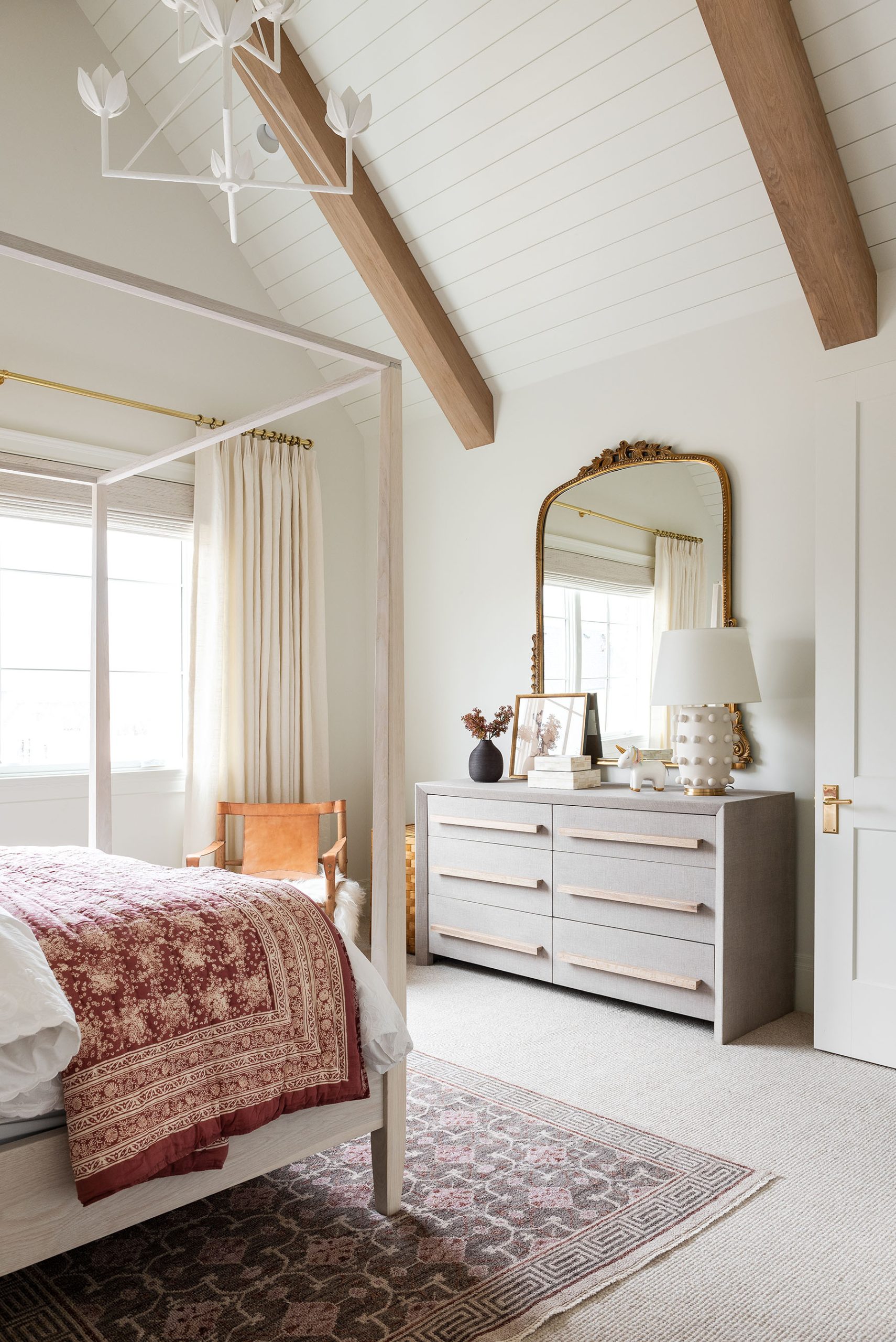 white bedroom with canopy bed and dresser with mirror and lamp
