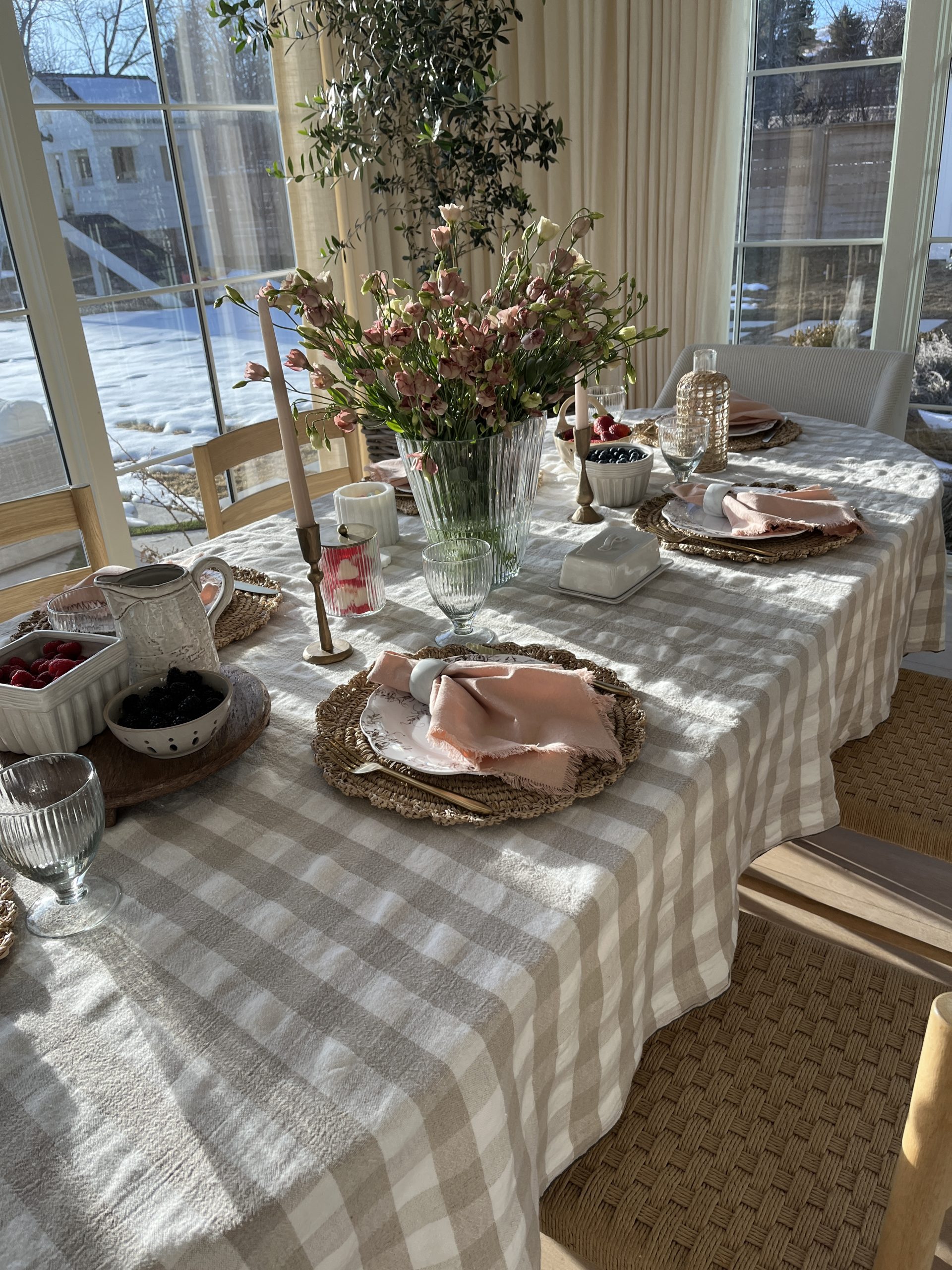 valentine's tablescape with floral arrangement, berries, servware, gingham tablecloth, woven placement, white plates, and pink napkins