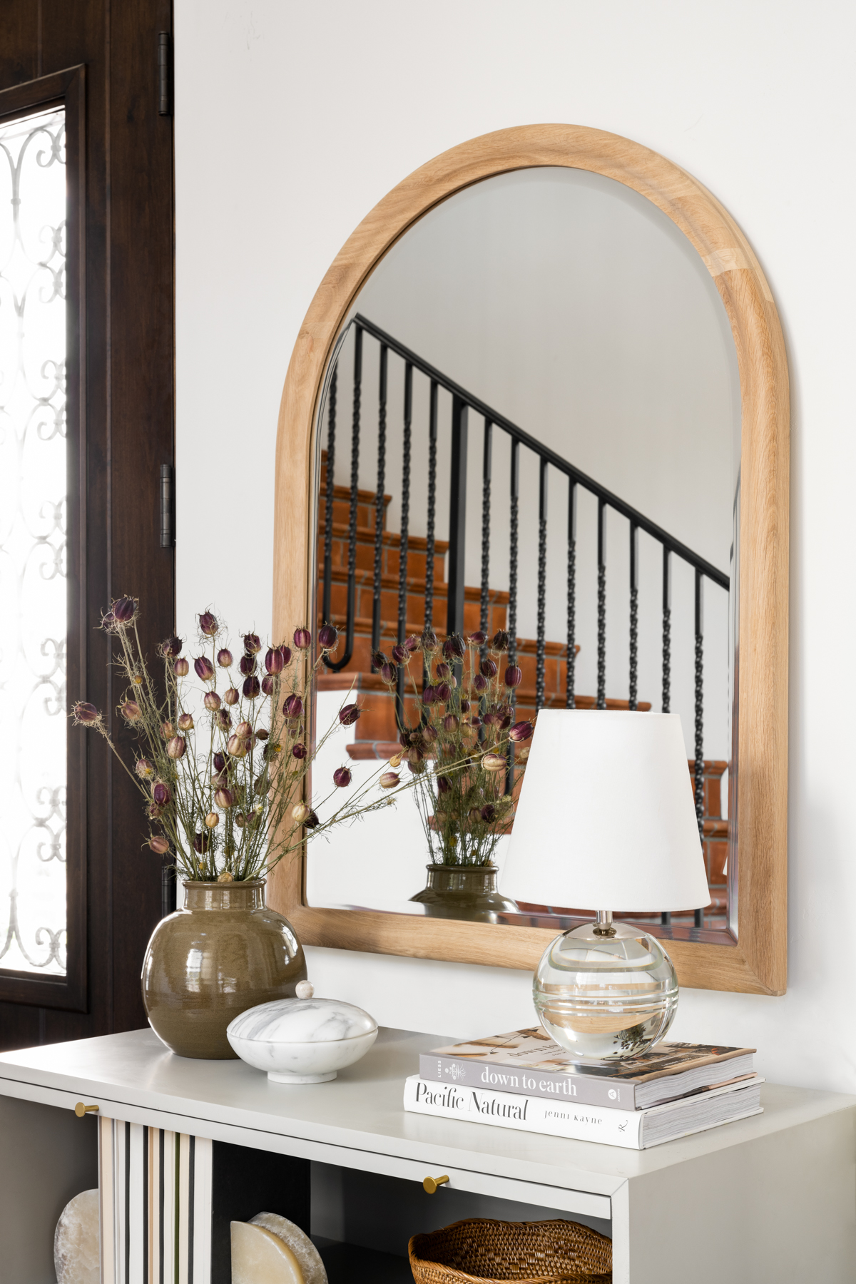console table with small green vase in front of arched mirror