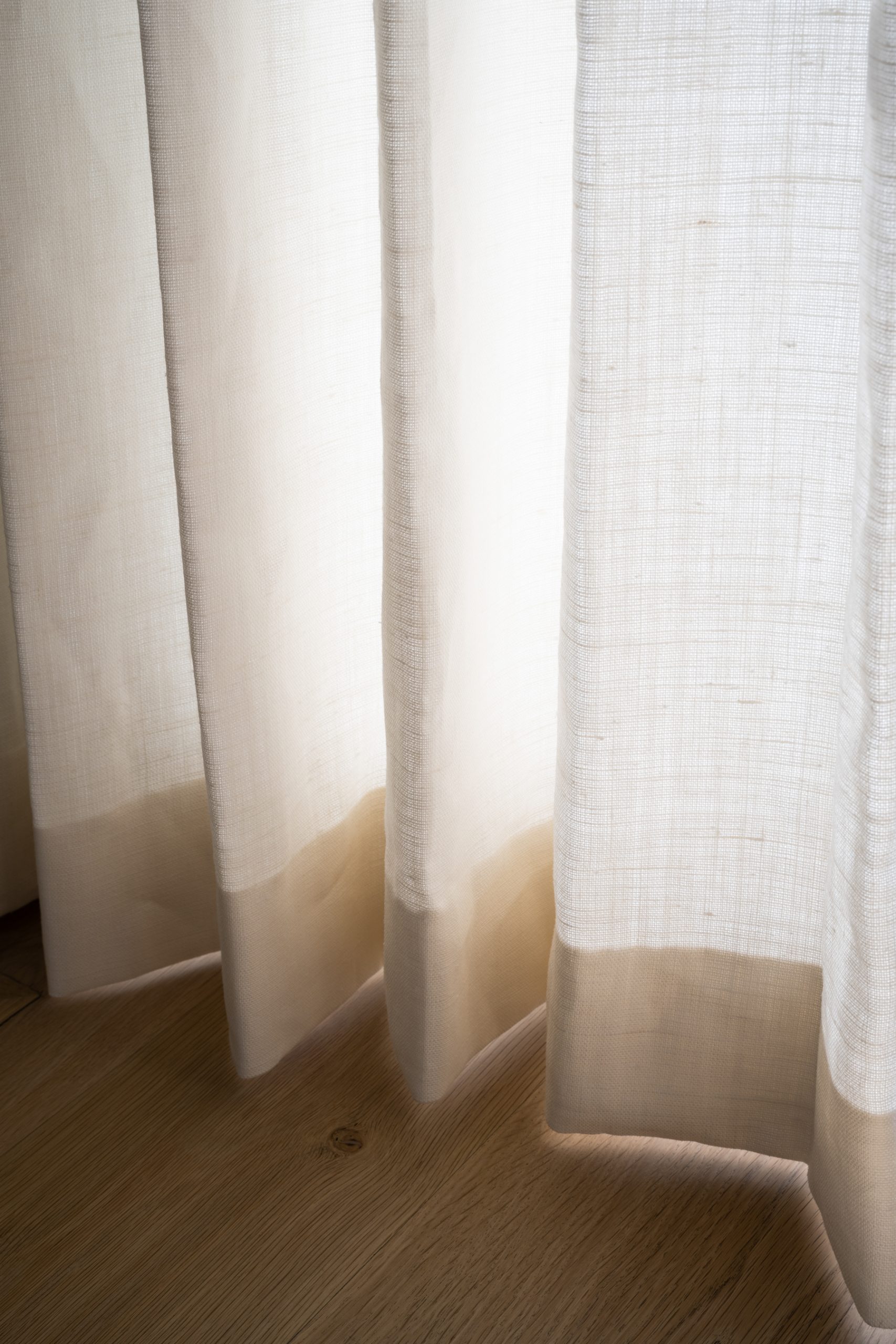 white pleated curtains hanging above wood floor