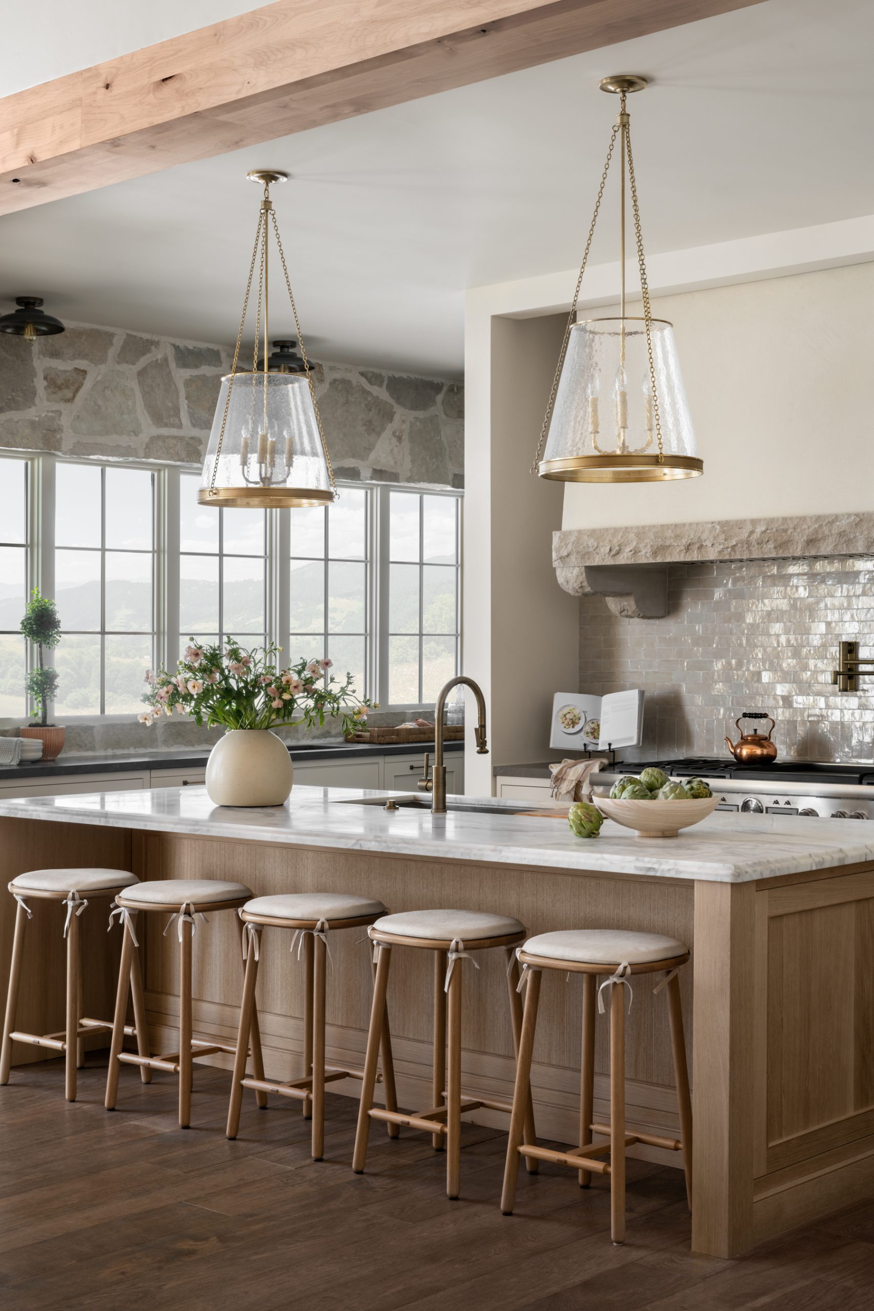 kitchen with natural wood island and marble countertops with wooden stools and glass pendants