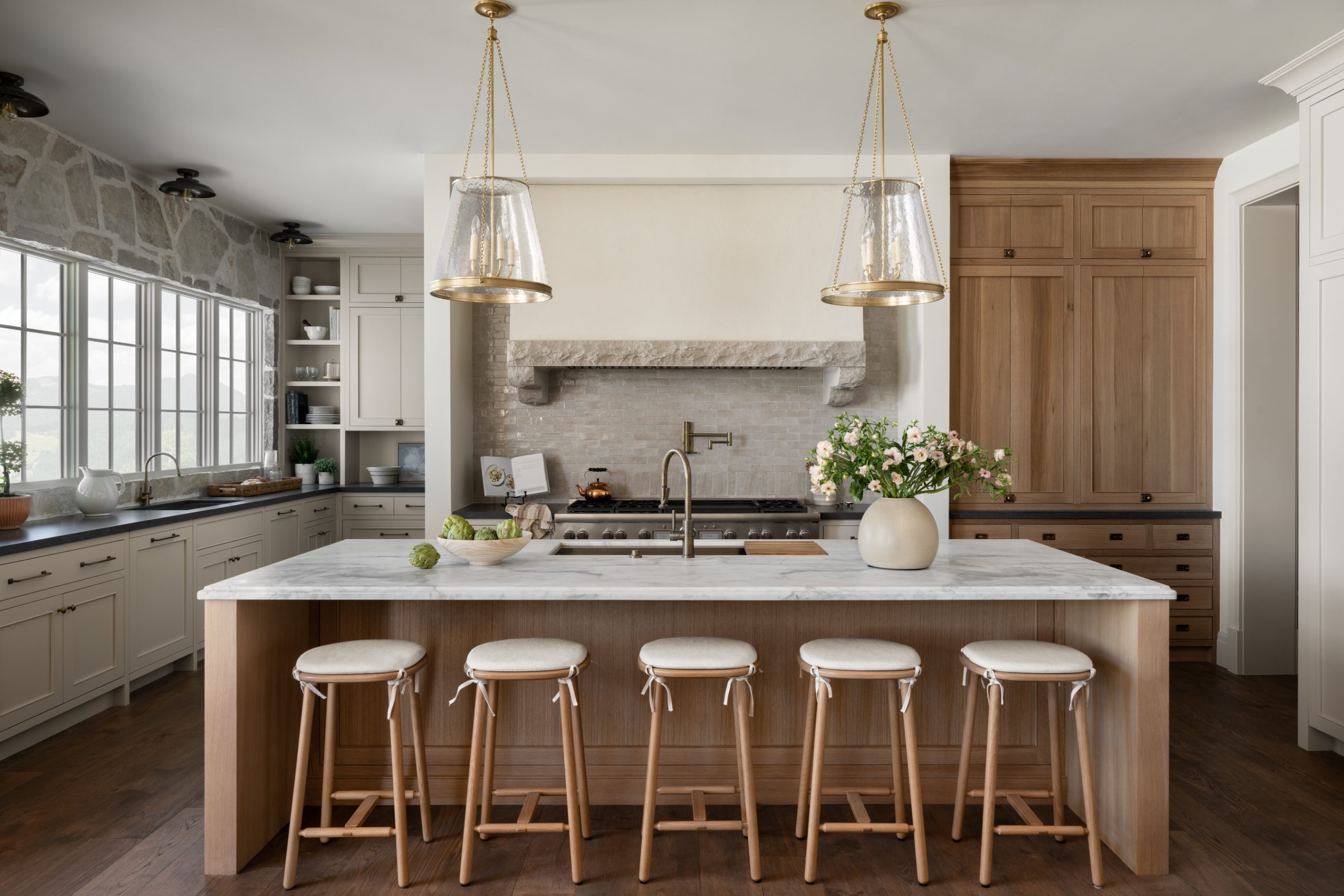 kitchen with natural wood island and marble countertops with wooden stools and glass pendants