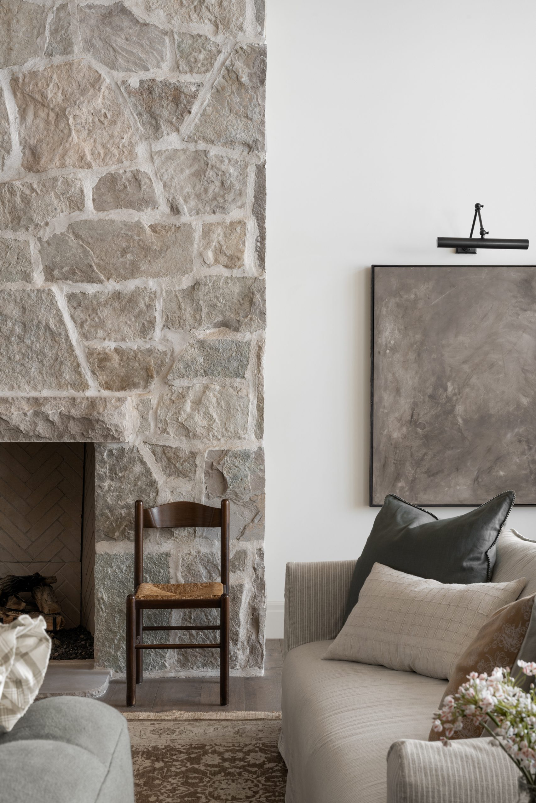 living room with stone fireplace and chair next to artwork with picture light