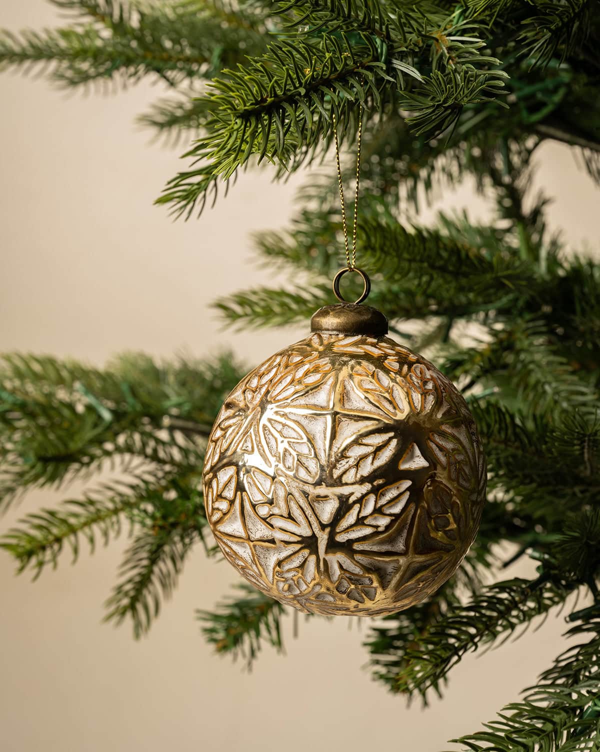 White and gold leaf design on the Alessandro glass bulb ornament hanging from a Christmas tree from Studio McGee.