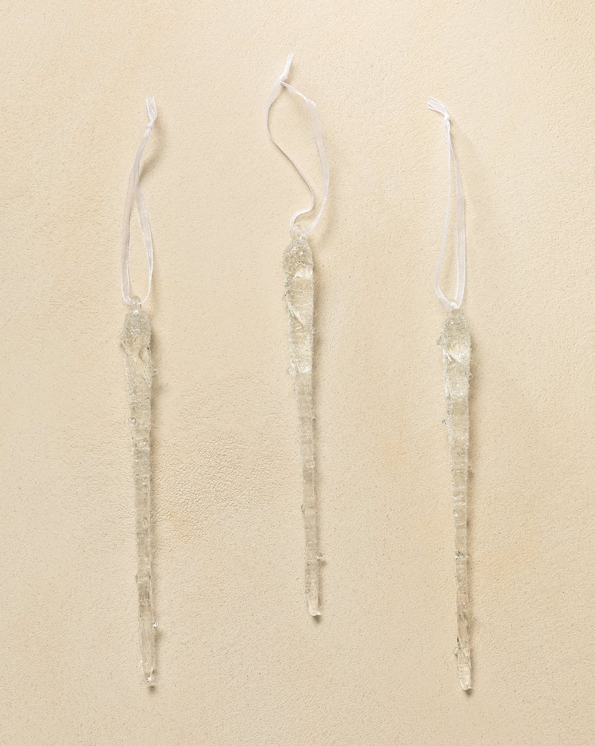 Set of 3 icicle ornaments made from transparent glass with white ribbons to hang from trees from Studio McGee.