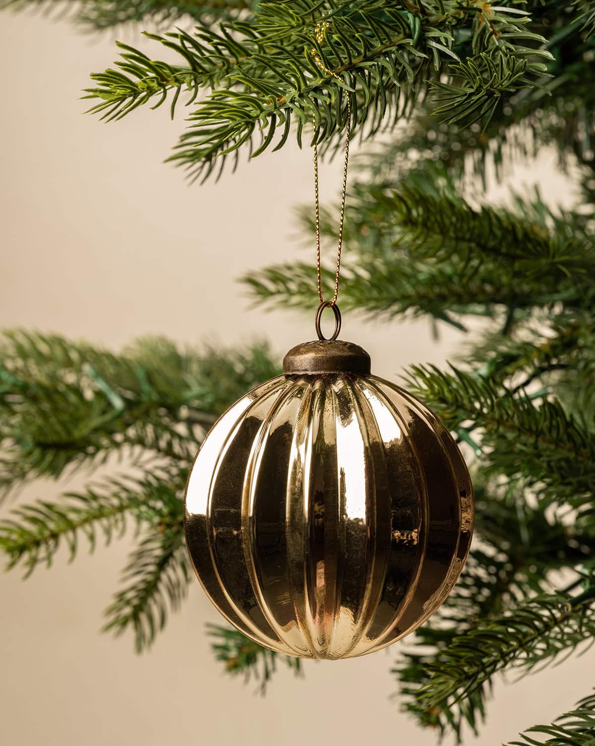 3" gold bauble holiday ornament hanging from a Christmas tree from a gold threaded holder from Studio McGee.
