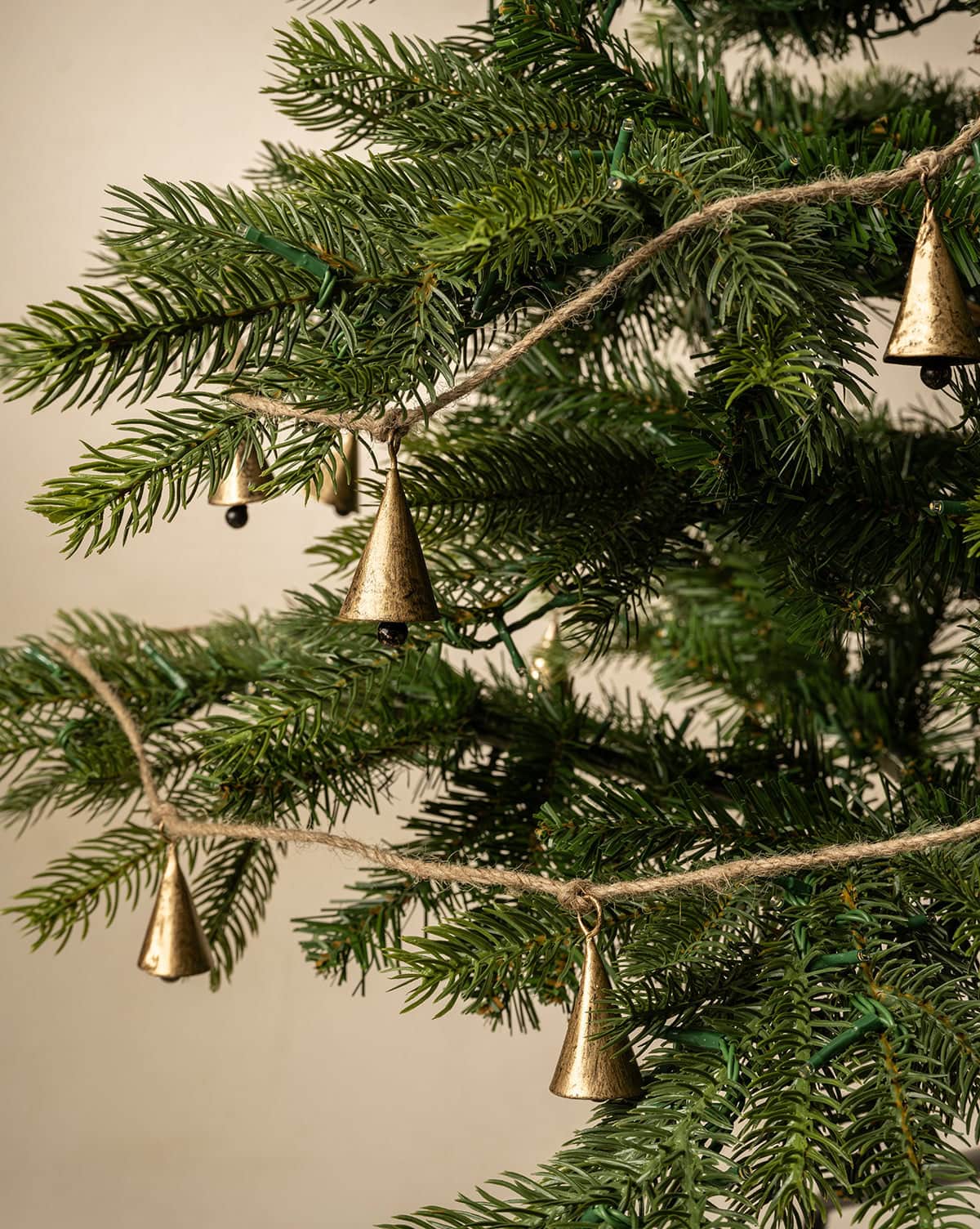 Antique-finished small gold cones hang from a roped garland shown on a spruce Christmas tree from Studio McGee.