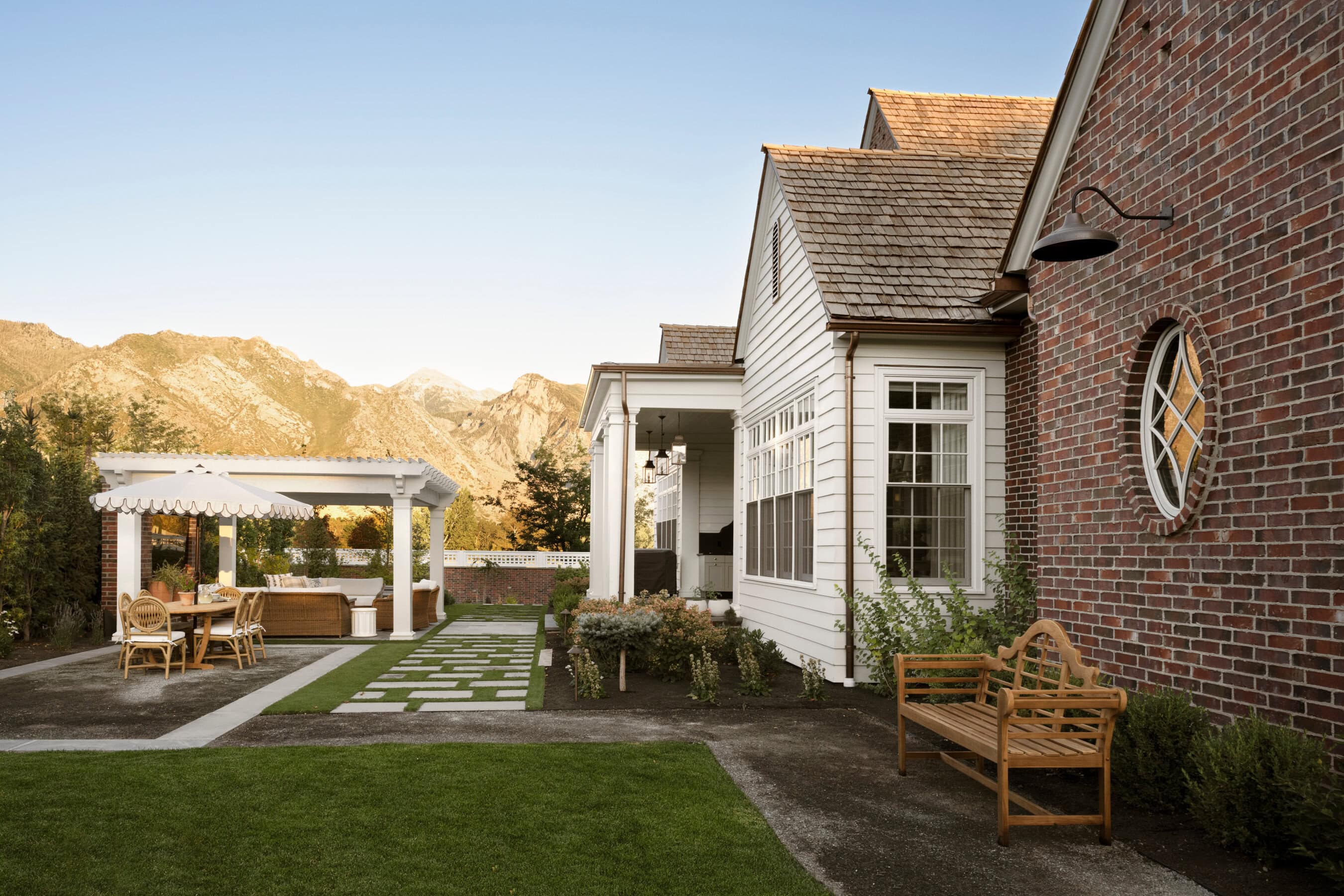 A house with a beautiful landscaped lawn with garden benches under pergolas from Studio McGee.