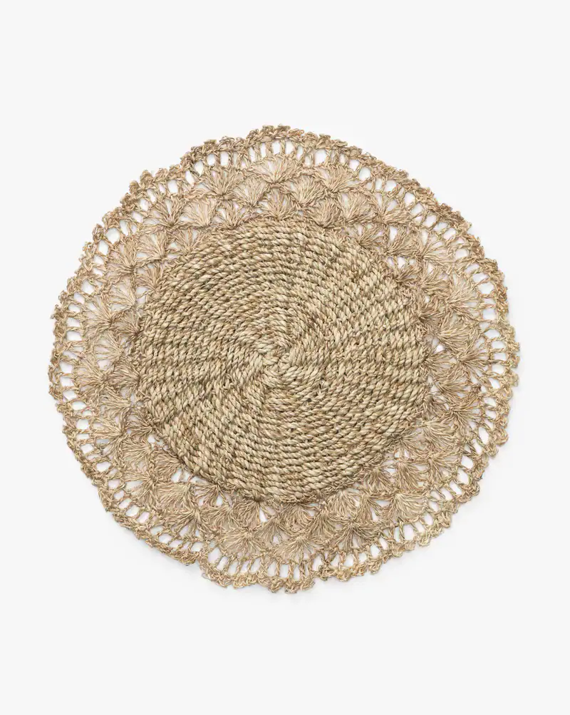Round woven placemat made of natural fibers with a braided center and an intricate, lacy outer edge, displayed on a white background, by McGee & Co.